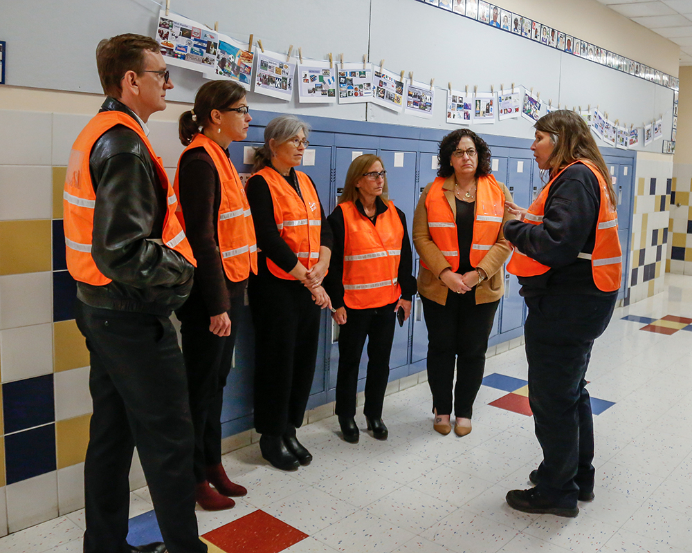 a group in orange safety vests talks in a school hallway